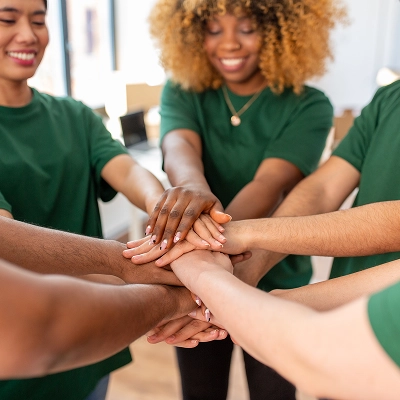 Group of teens wearing green shirts putting their hands in the middle of a circle like a team