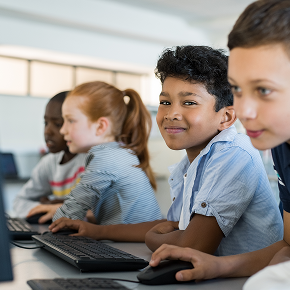 Group of kids sitting at desks with computers working in school