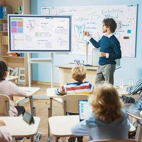 teacher at the front of an elementary school classroom with kids sitting at their desks